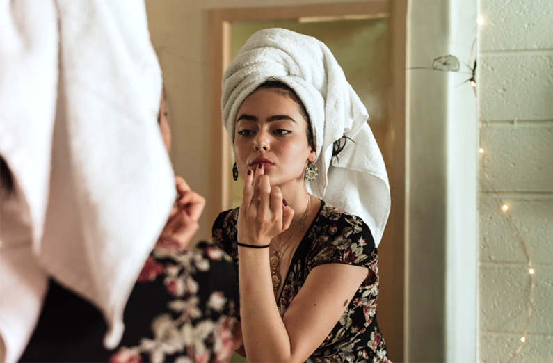 Wedding Makeup - Woman Dabbing On Lipstick In The Mirror With Wrapped Hair
