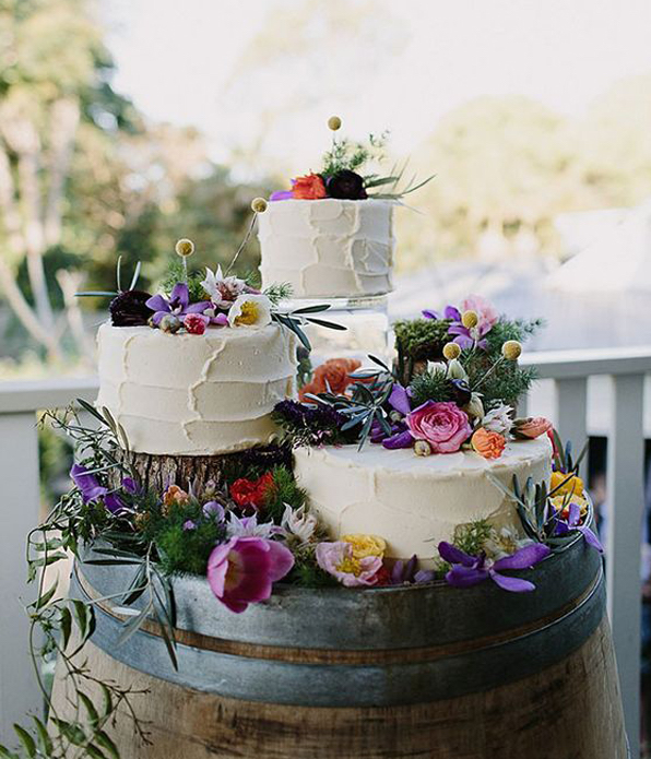 Three Separate Wedding Cakes Decorated With Spring Flowers Sitting On Barrel